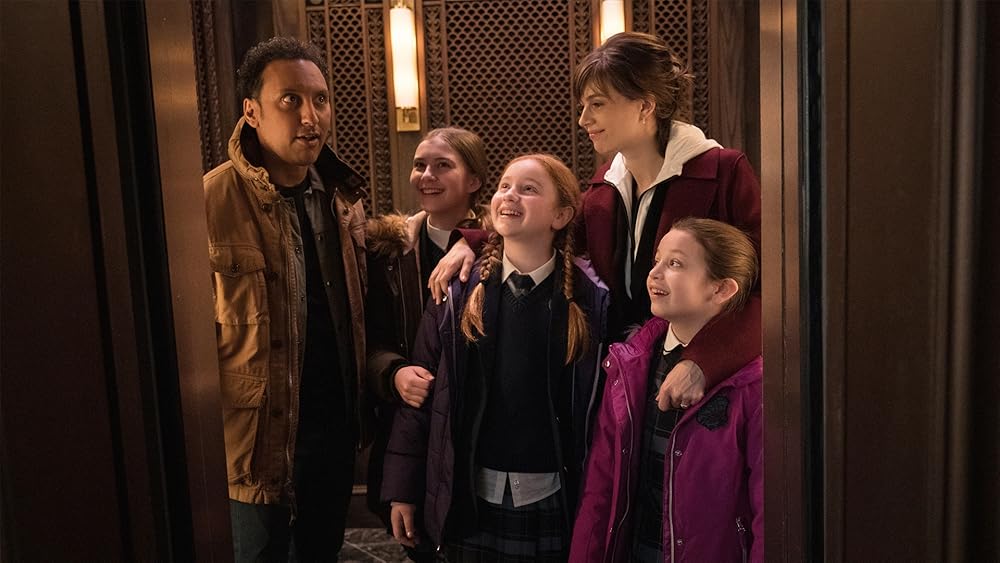 One man, three girls and one woman pile into an elevator, looking excited