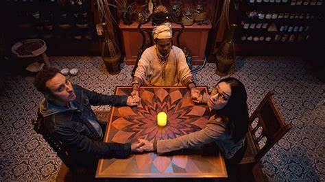 A medium holds hands with a couple as they sit on around a table. A candle rests before them.