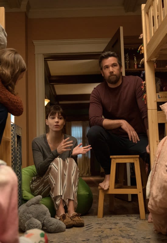 A woman and a man sit with their children. The man sits on a stool while the woman sits on a bean bag. 