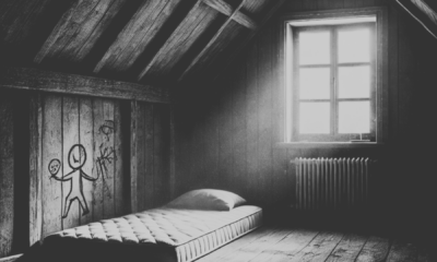 attic room with a small mattress on the floor, dim natural light streaming through a dusty window, and scratched walls featuring carvings of children playing. The atmosphere is eerie and evokes a sense of isolation and despair