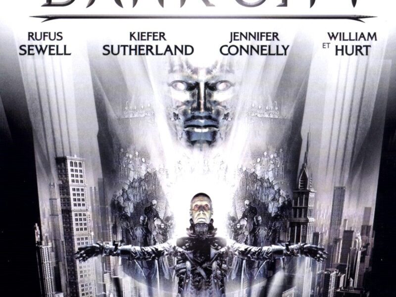 Dark City reads on a white background in silver text. A face forms from the city. Below it, a man stands in a crucified position.