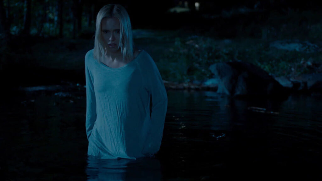 A woman emerges from a lake, looking into the water with visible confusion.