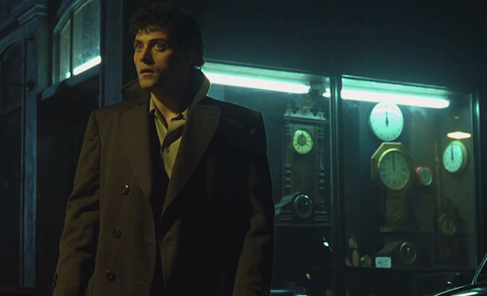 A man in a trench coat stares in the distance. Behind him is a case.