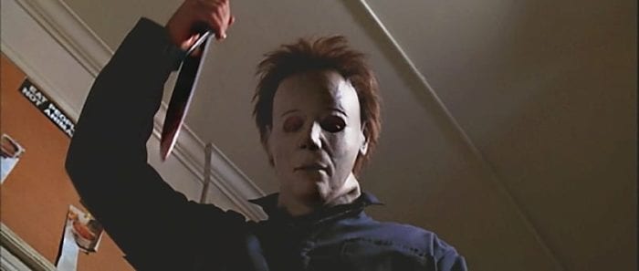 Michael Myers has a kitchen knife raised staring at something off-screen.