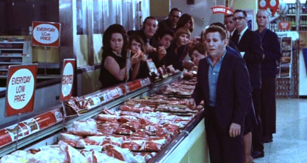 Several pale people stand over raw meat in a grocery store. It looks as though they are eating the meat raw.